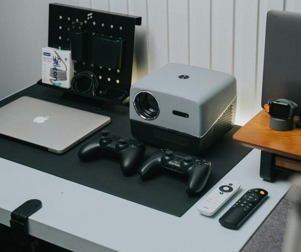 A sleek home office setup featuring a projector, game controllers, and laptop.
